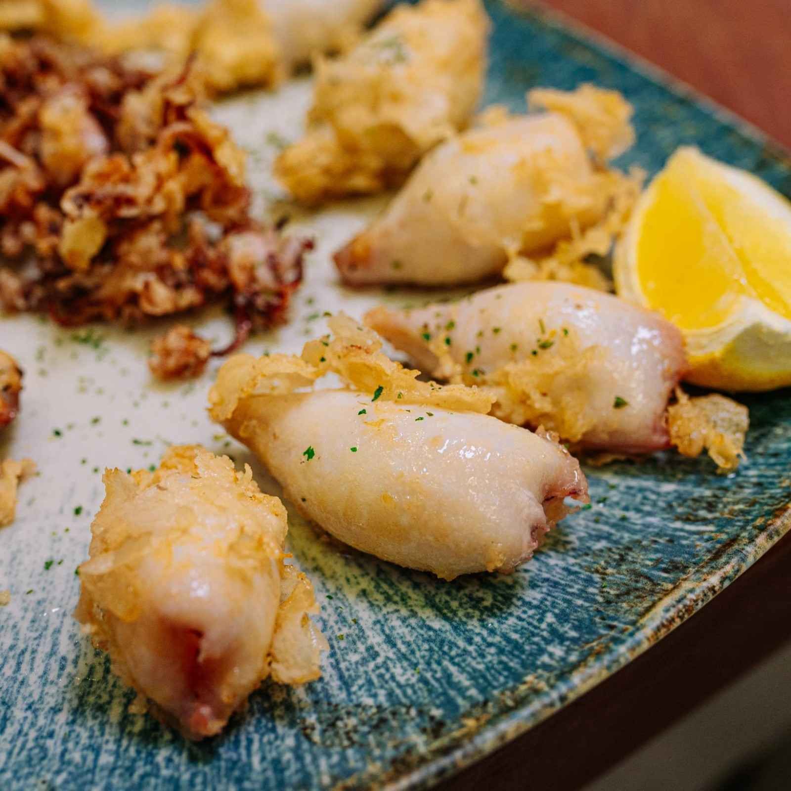 Plato de calamares a la parrilla con rodajas de limón y guarnición frita sobre un plato azul.