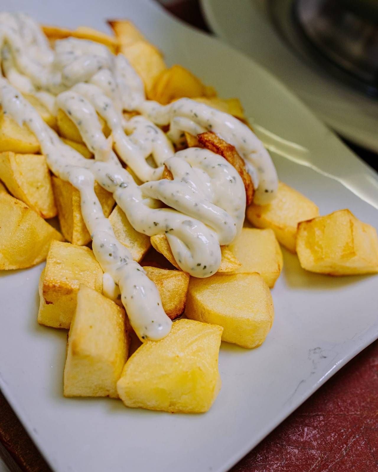 Papas fritas cubiertas con salsa blanca cremosa en un plato blanco.