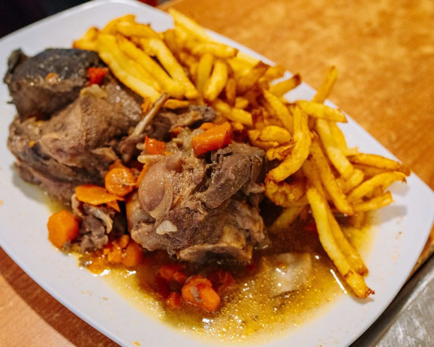 Ternera emplatada con patatas fritas y zanahorias en dados en salsa marrón sobre un plato blanco.