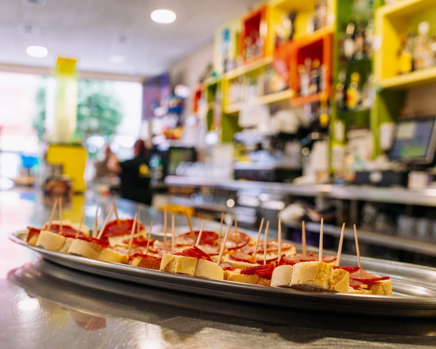 Platos de aperitivos del tamaño de un bocado con palillos de dientes sobre el mostrador de una cafetería o bar luminoso.
