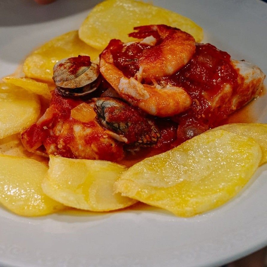 Pasta con salsa de tomate rojo y gambas en un plato blanco, rodeada de rodajas de patata amarilla.