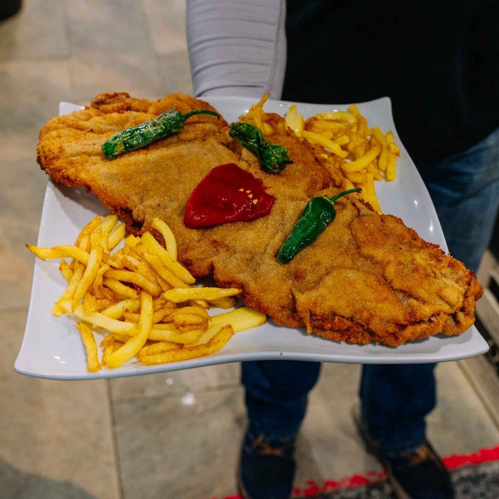 Pescado frito empanizado en una bandeja con papas fritas, guisantes y kétchup.