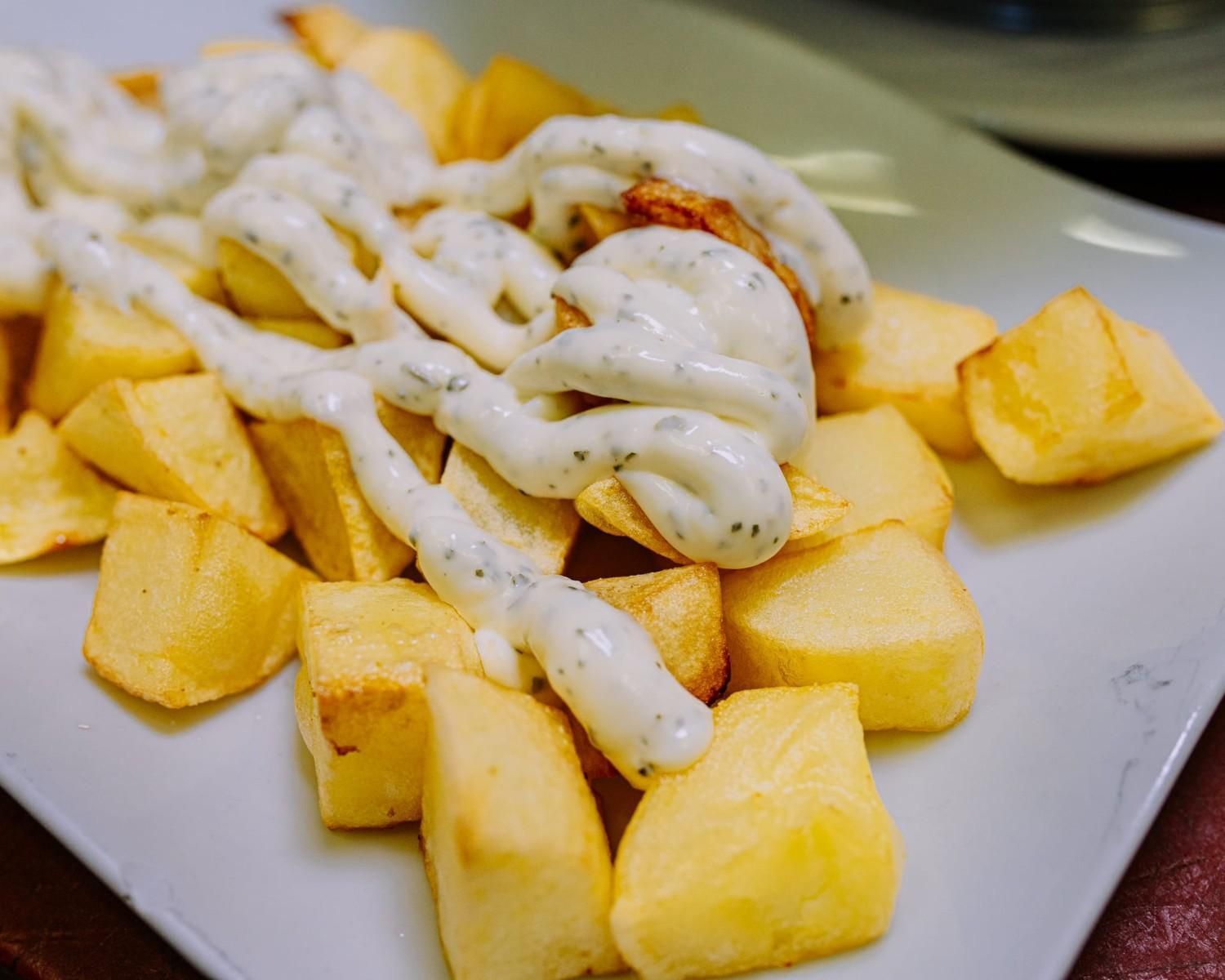 Plato de patatas gajo doradas cubiertas con una salsa blanca cremosa.