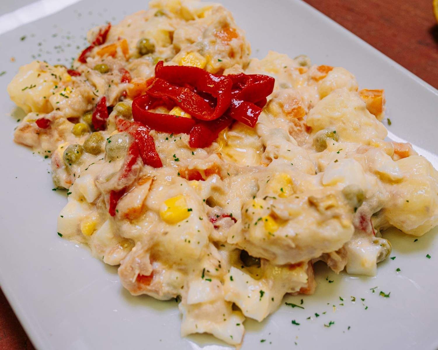Ensalada cremosa de patatas con rodajas de pimiento rojo sobre un plato blanco.