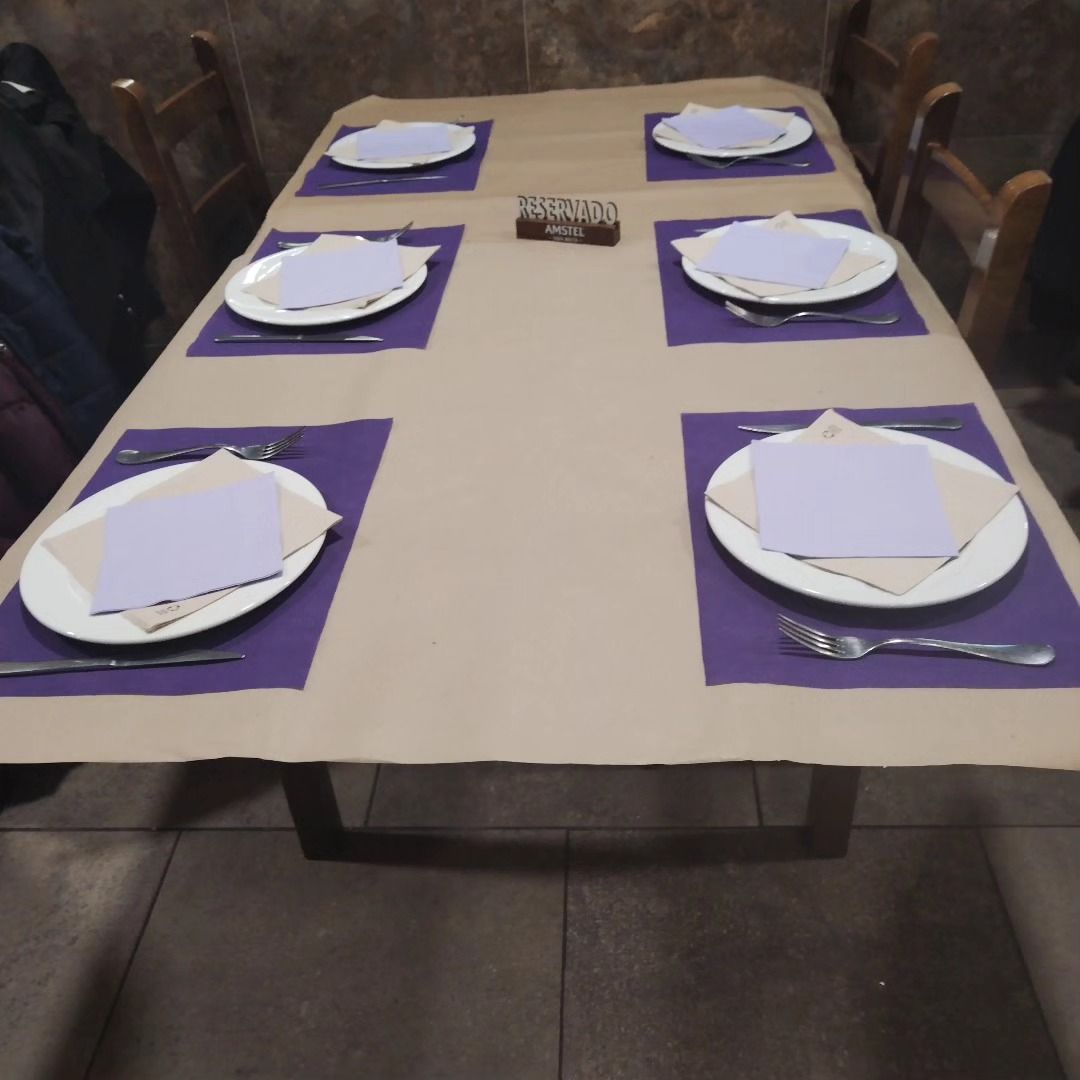 Prepara la mesa del comedor con manteles individuales morados, platos blancos y servilletas dobladas.