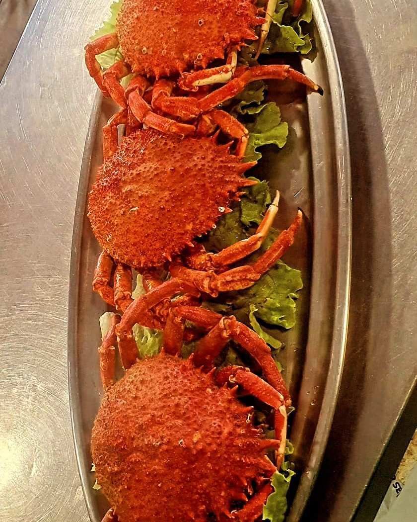 Tres cangrejos rojos cocidos dispuestos en una bandeja de plata con guarnición verde.