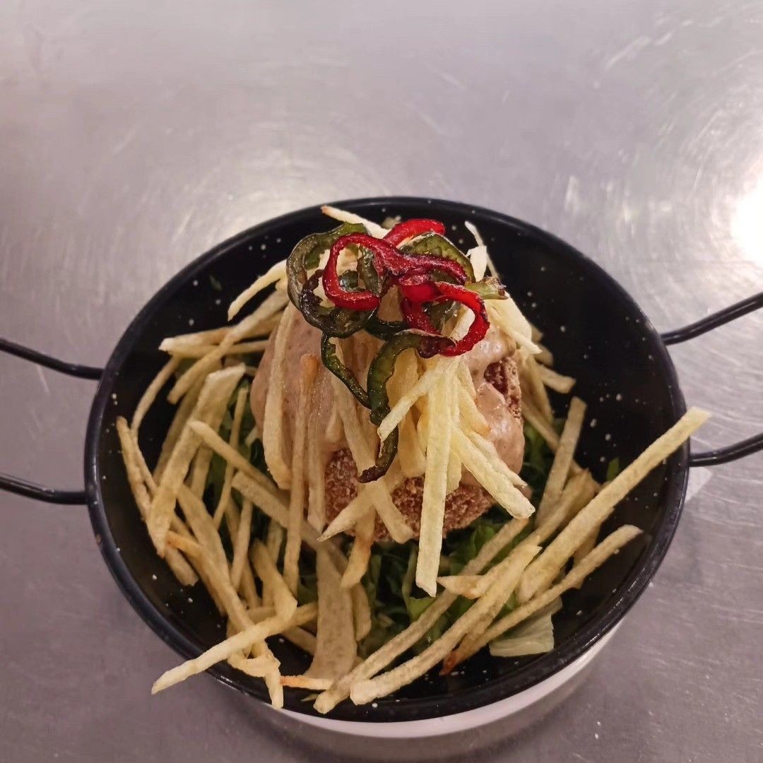 Un tazón de ensalada de fideos con rodajas de chile y hierbas sobre una mesa de metal.