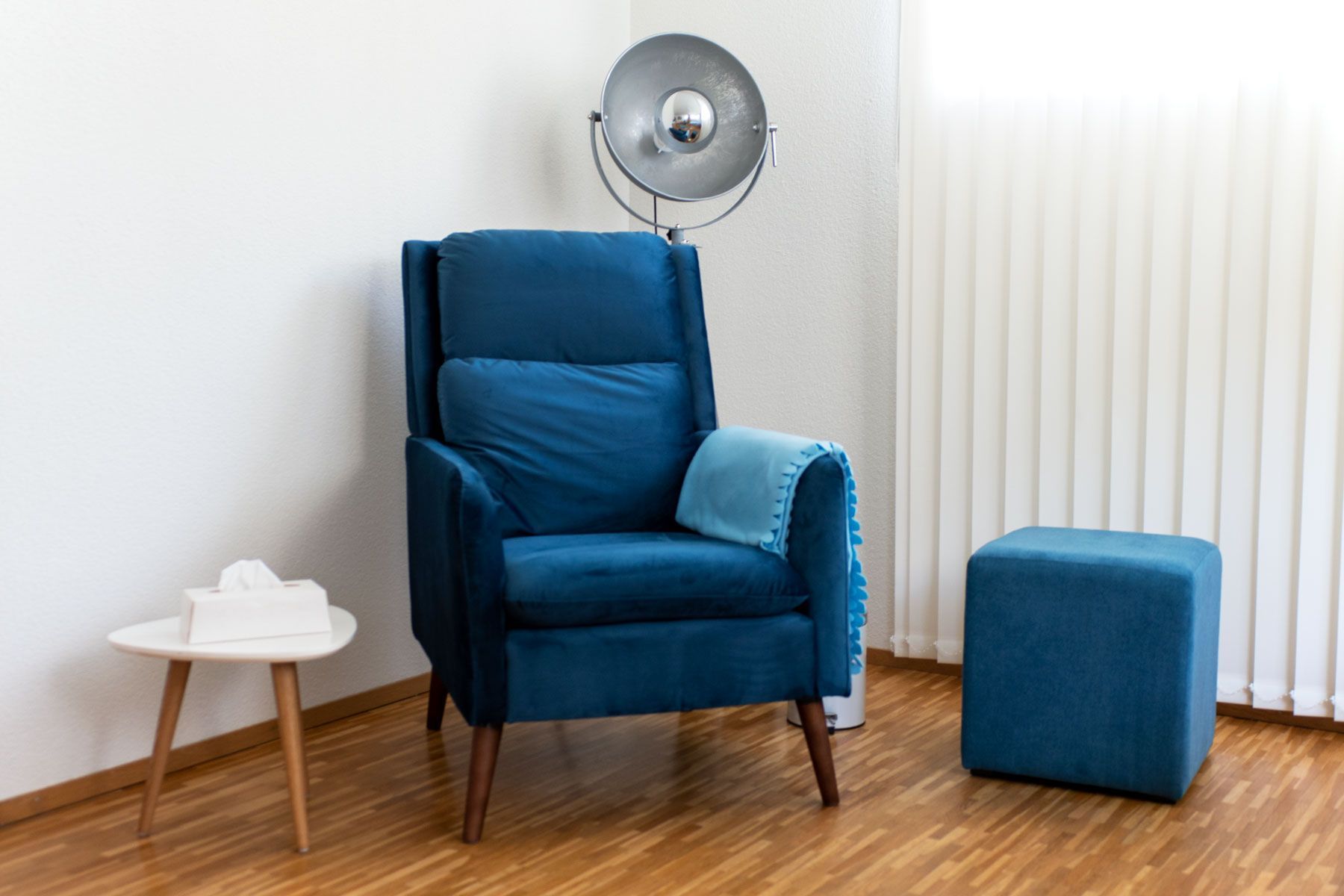 Ein blauer Sessel und ein Ottomane stehen in einem Raum neben einem Fenster.