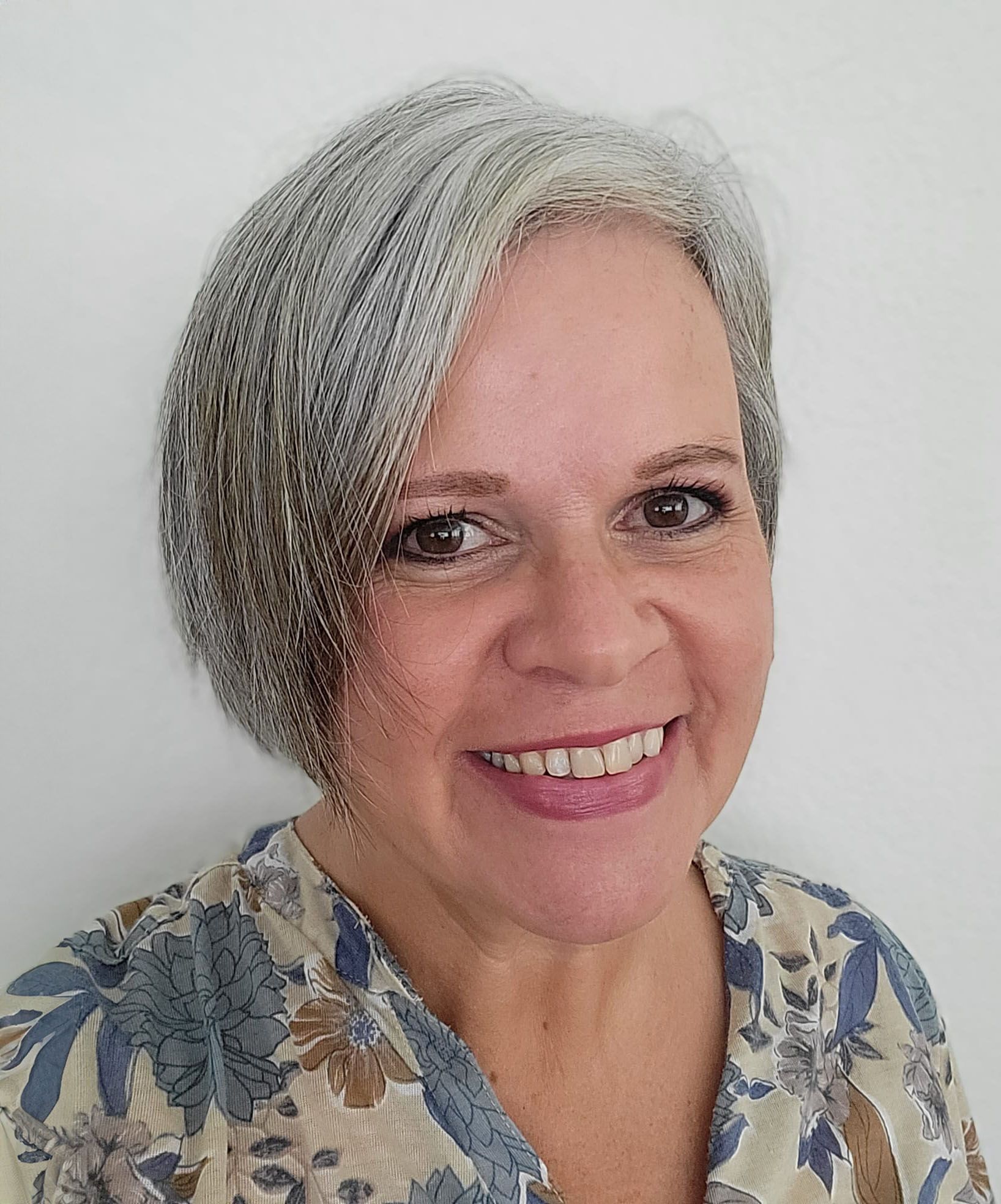 Eine Frau mit grauem Haar lächelt und trägt ein geblümtes Hemd.