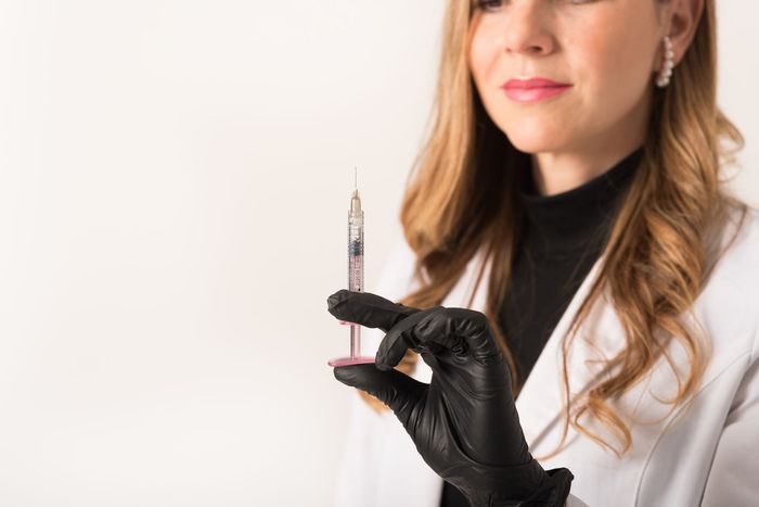 Mujer con bata de laboratorio y guantes sosteniendo una jeringa.