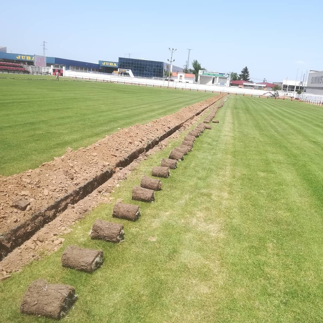 Una larga zanja cavada en un campo verde; junto a ella hay rollos de césped.