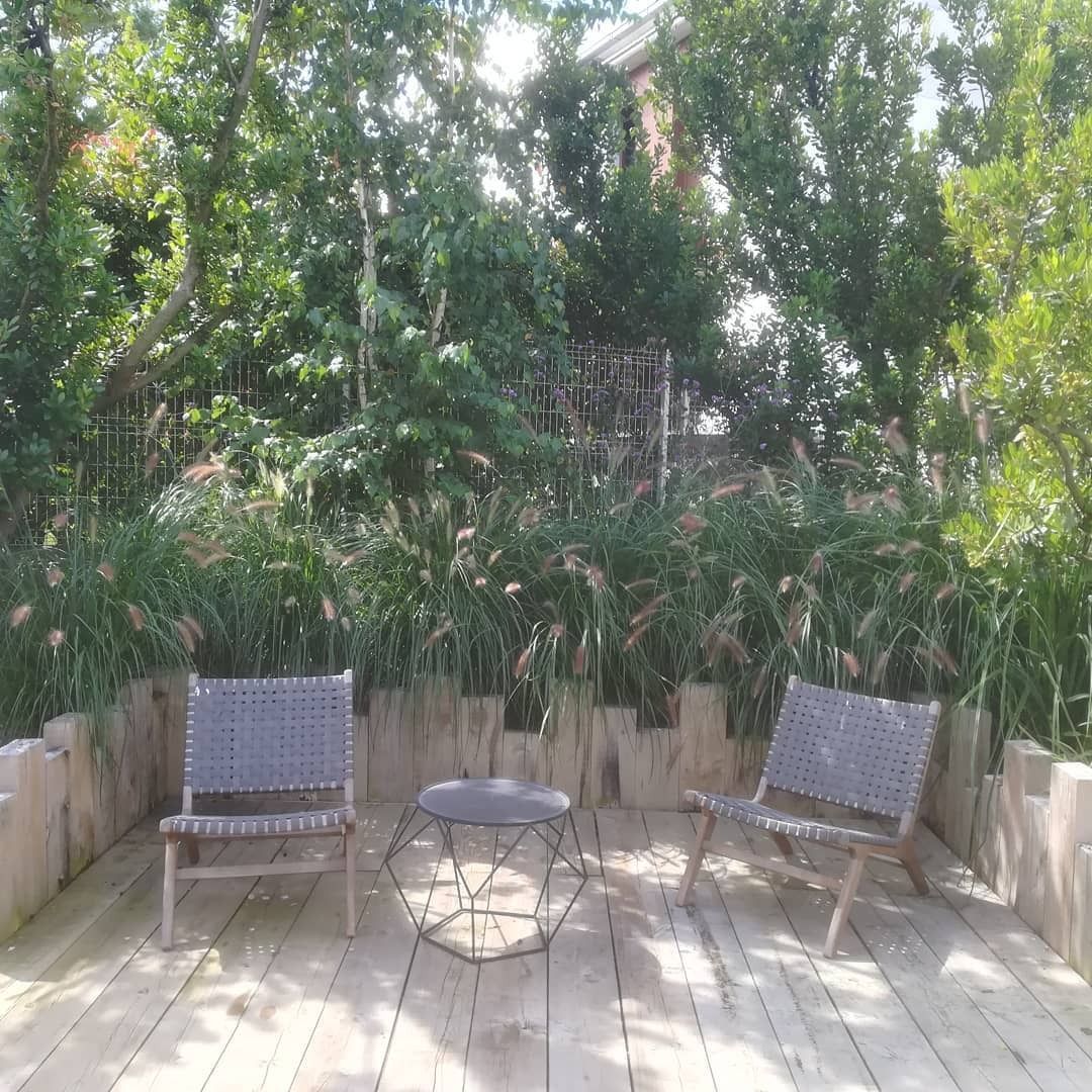 Dos sillas y una mesa pequeña en un deck de madera, con una exuberante vegetación al fondo.