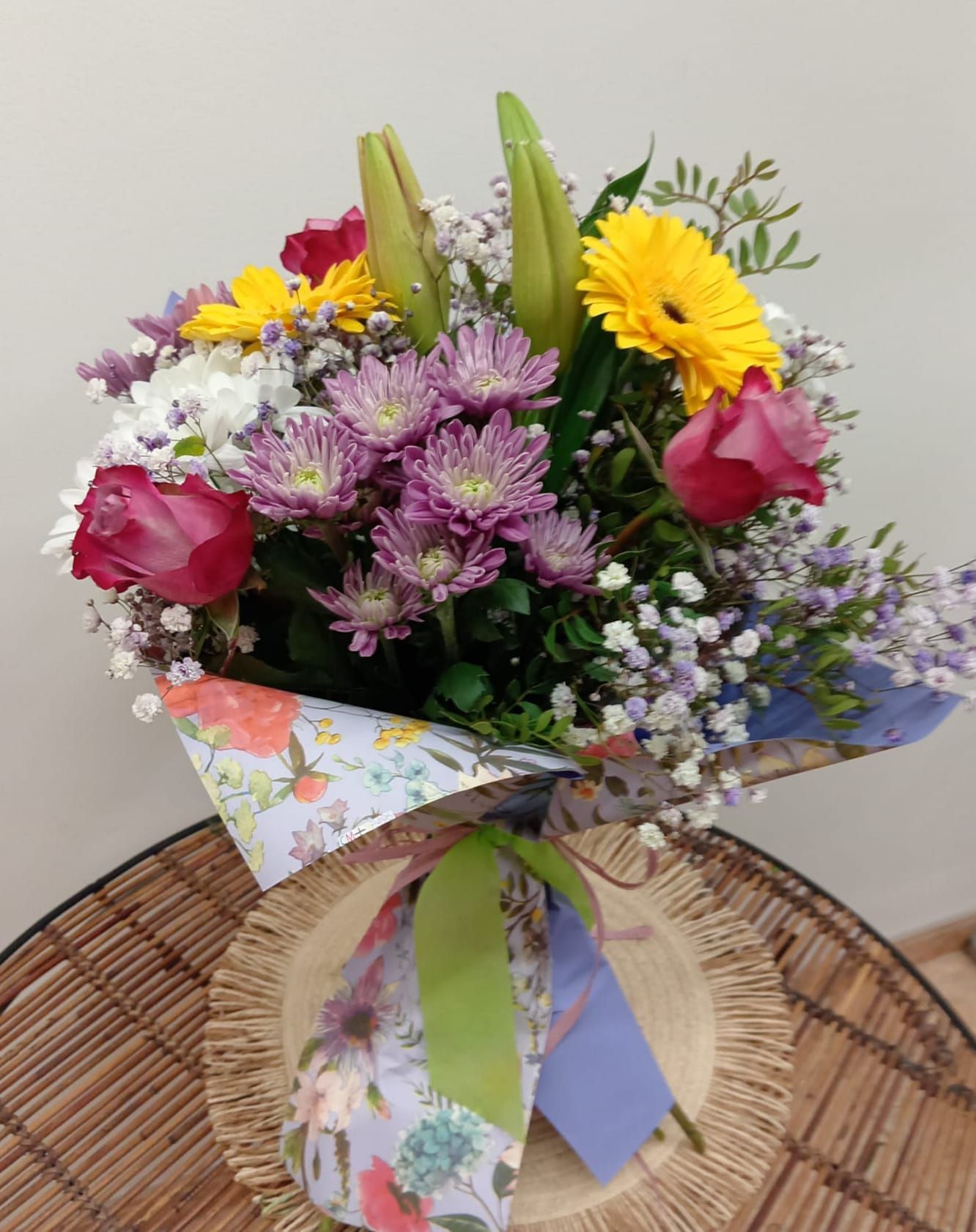 Un ramo de flores envuelto en papel floral está sobre una mesa.
