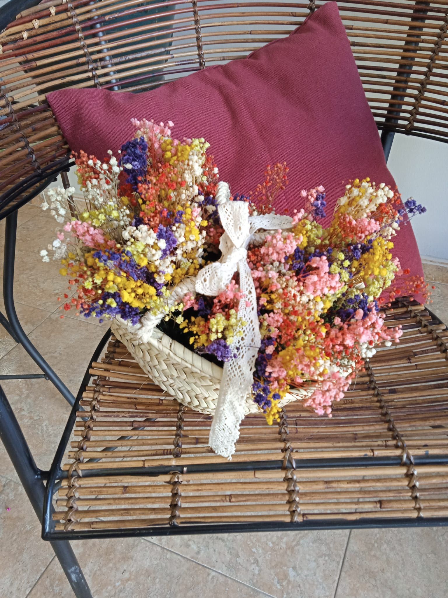 Una cesta de flores secas está sobre una silla al lado de una almohada.
