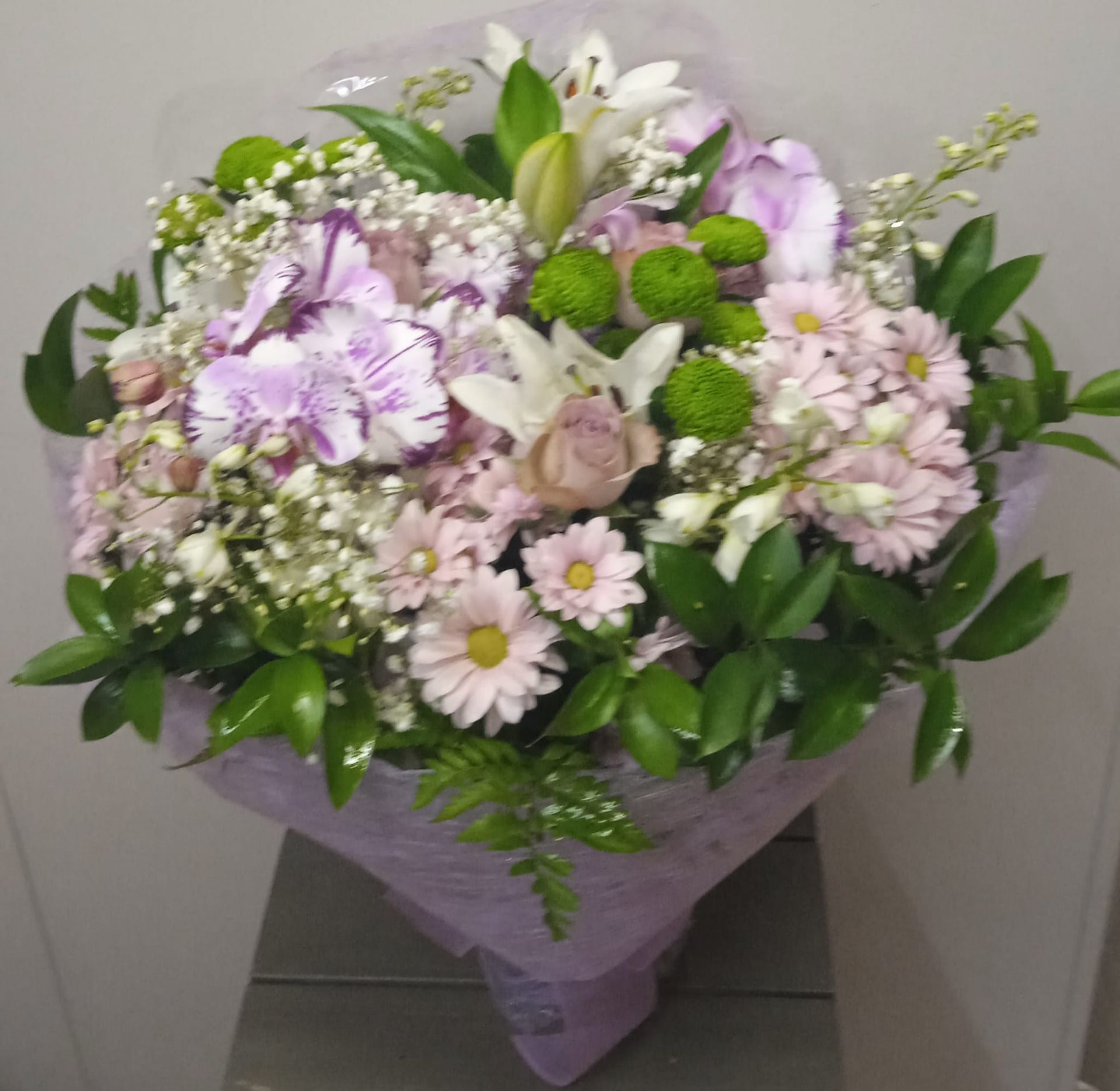 Un ramo de flores rosas y blancas envuelto en papel morado.