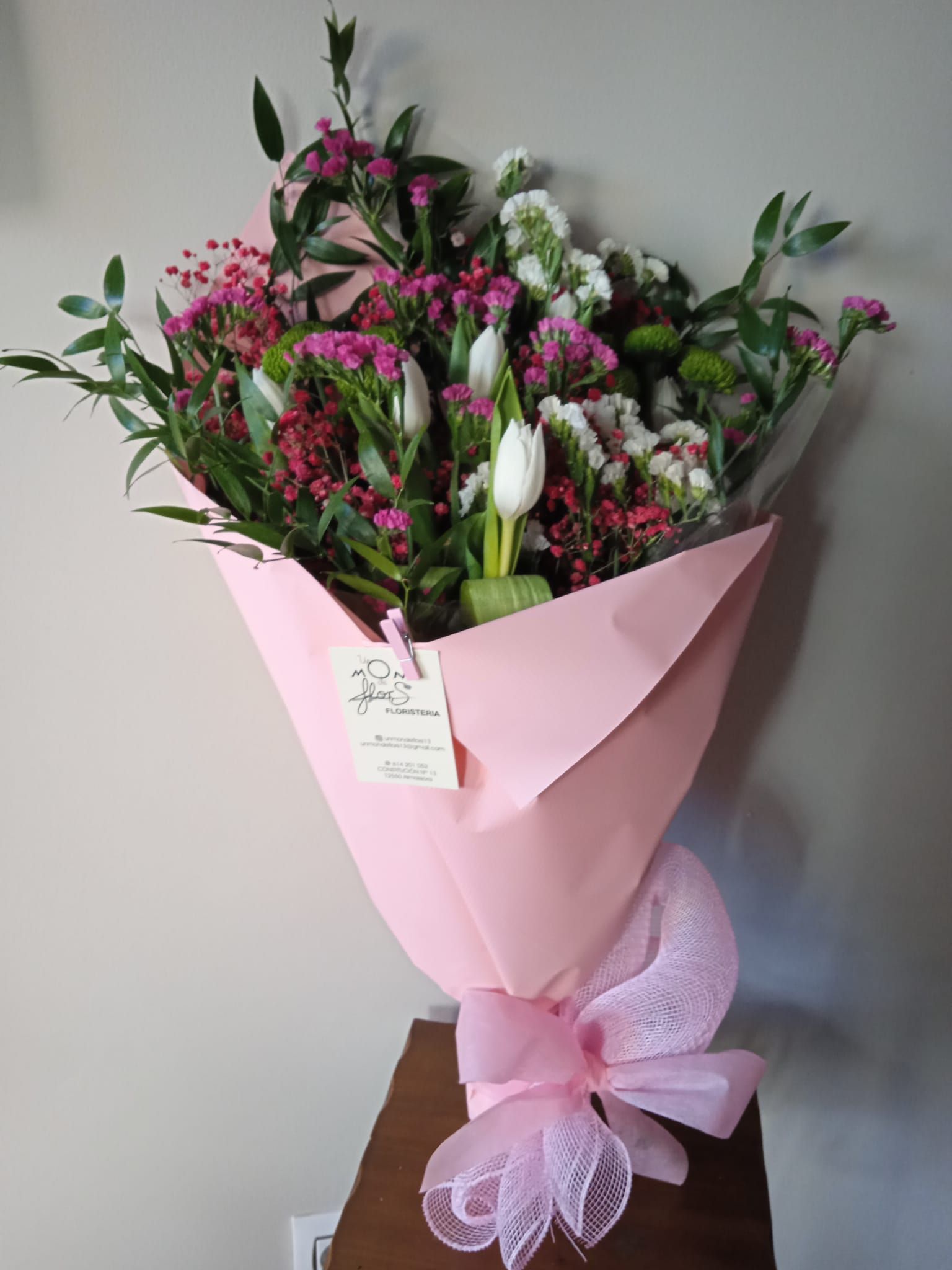 Un ramo de flores rosas y blancas envuelto en papel rosa sobre una mesa.