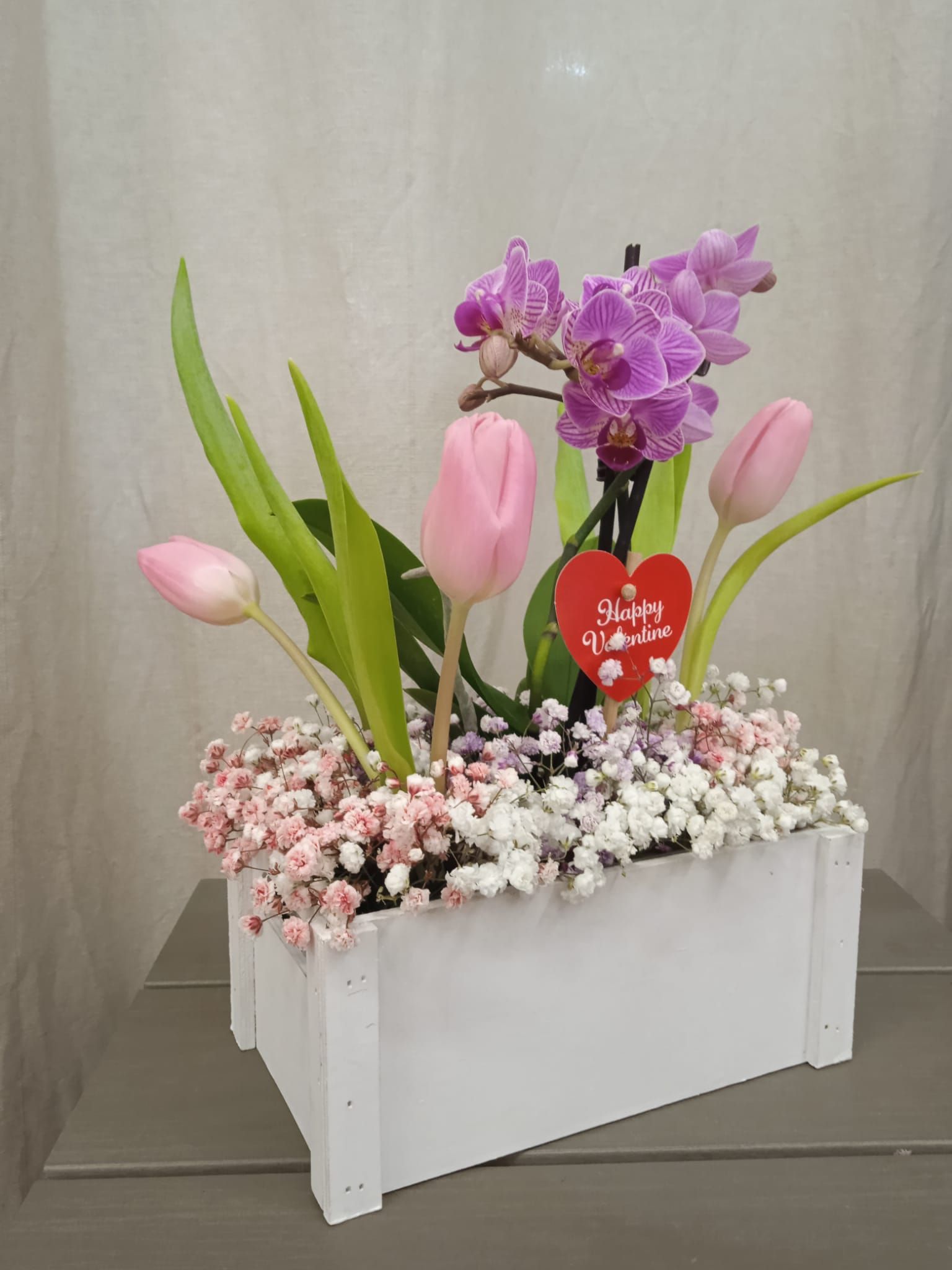 Una caja de madera blanca llena de flores y un corazón.