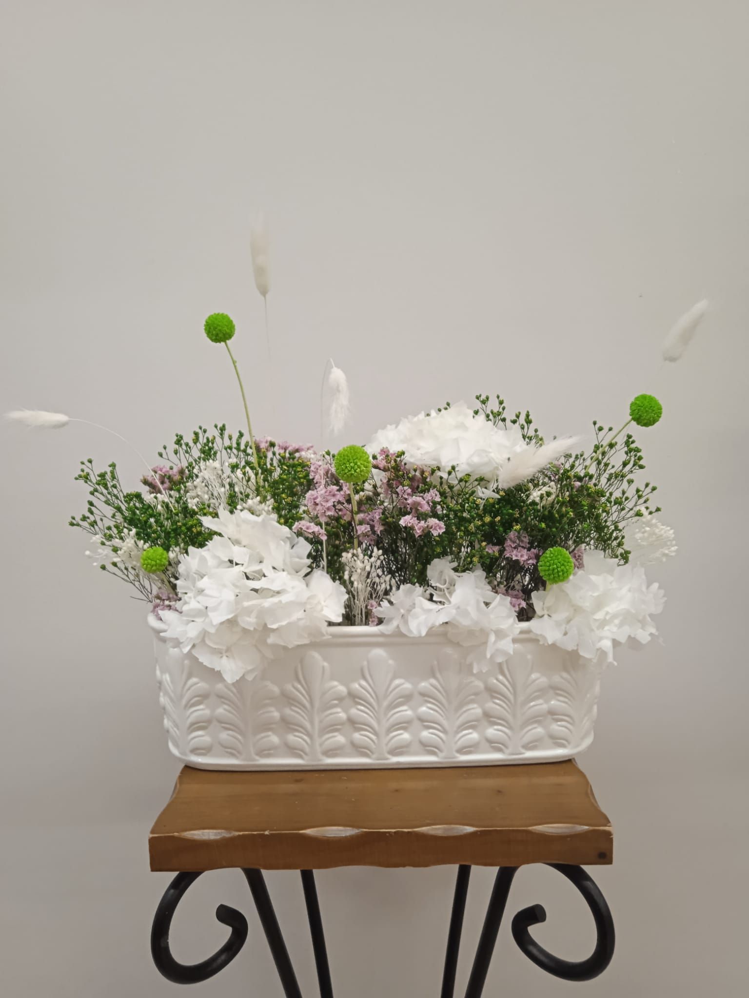 Una canasta blanca llena de flores está sobre una mesa de madera.