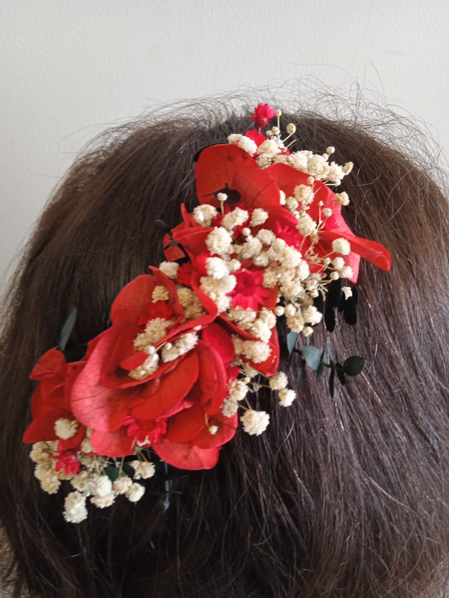 El cabello de una mujer está decorado con flores rojas y aliento de bebé.