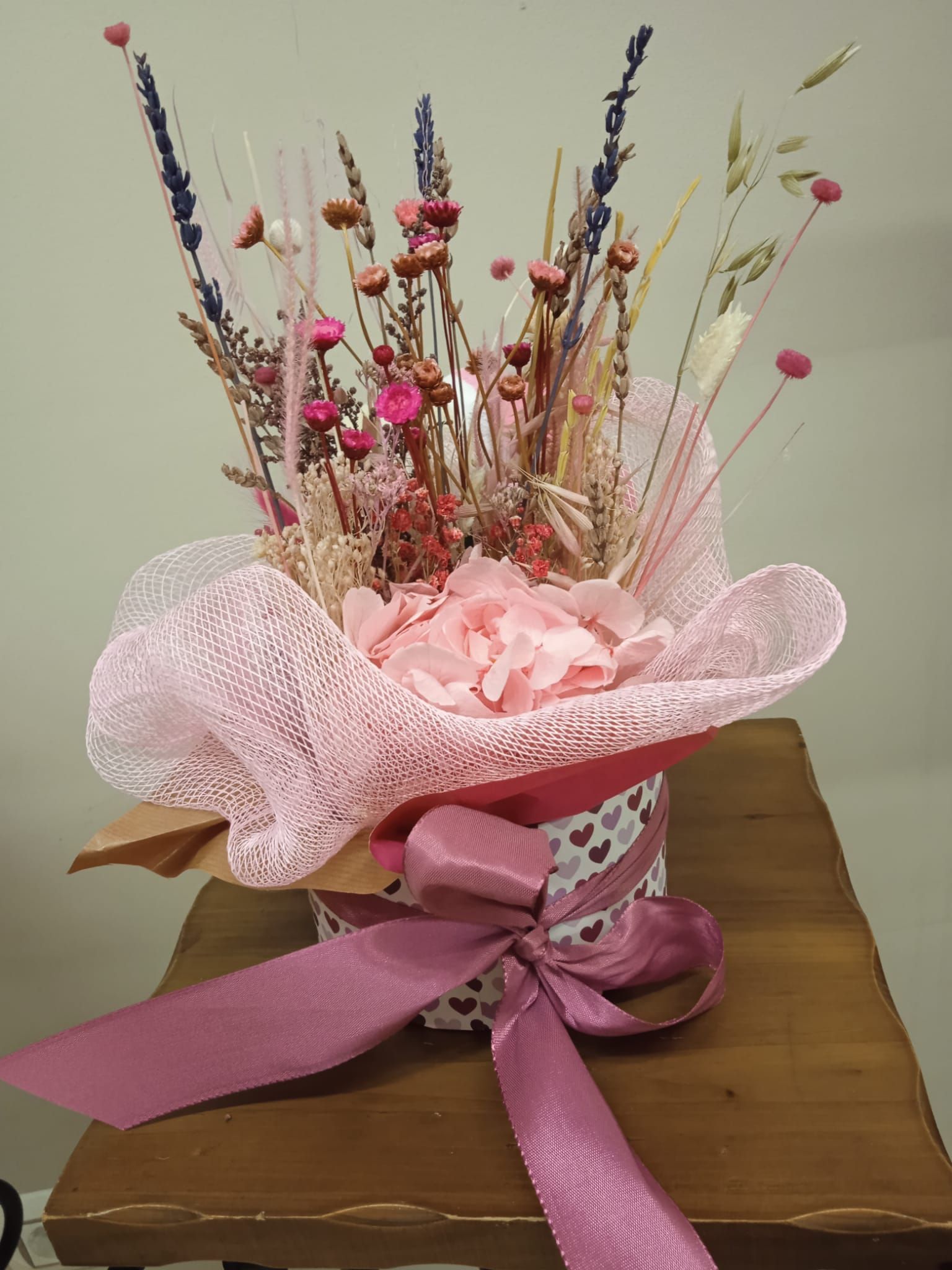 Un jarrón lleno de flores secas está sobre una mesa de madera.