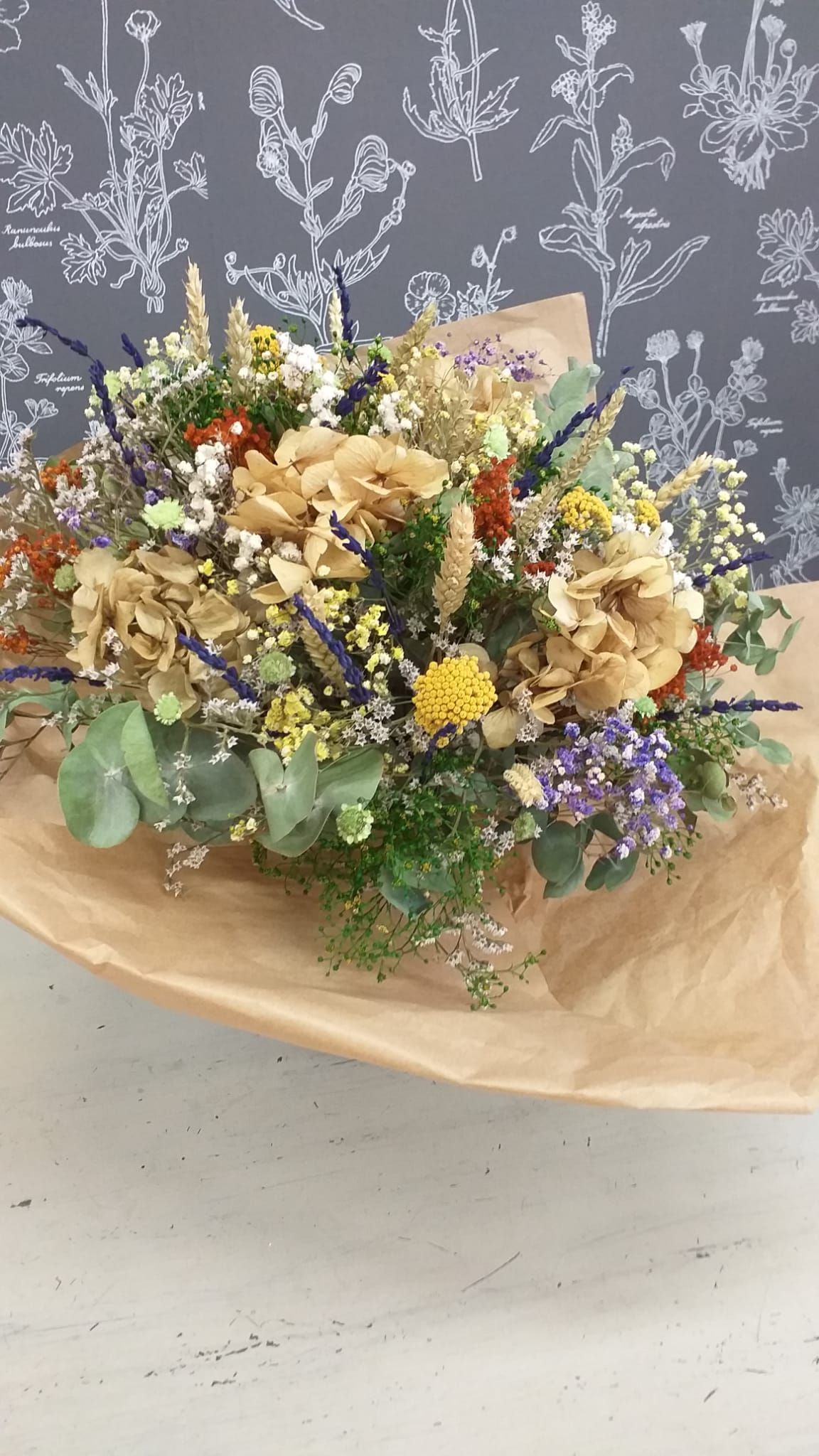 Un ramo de flores secas está envuelto en papel marrón y colocado sobre una mesa.