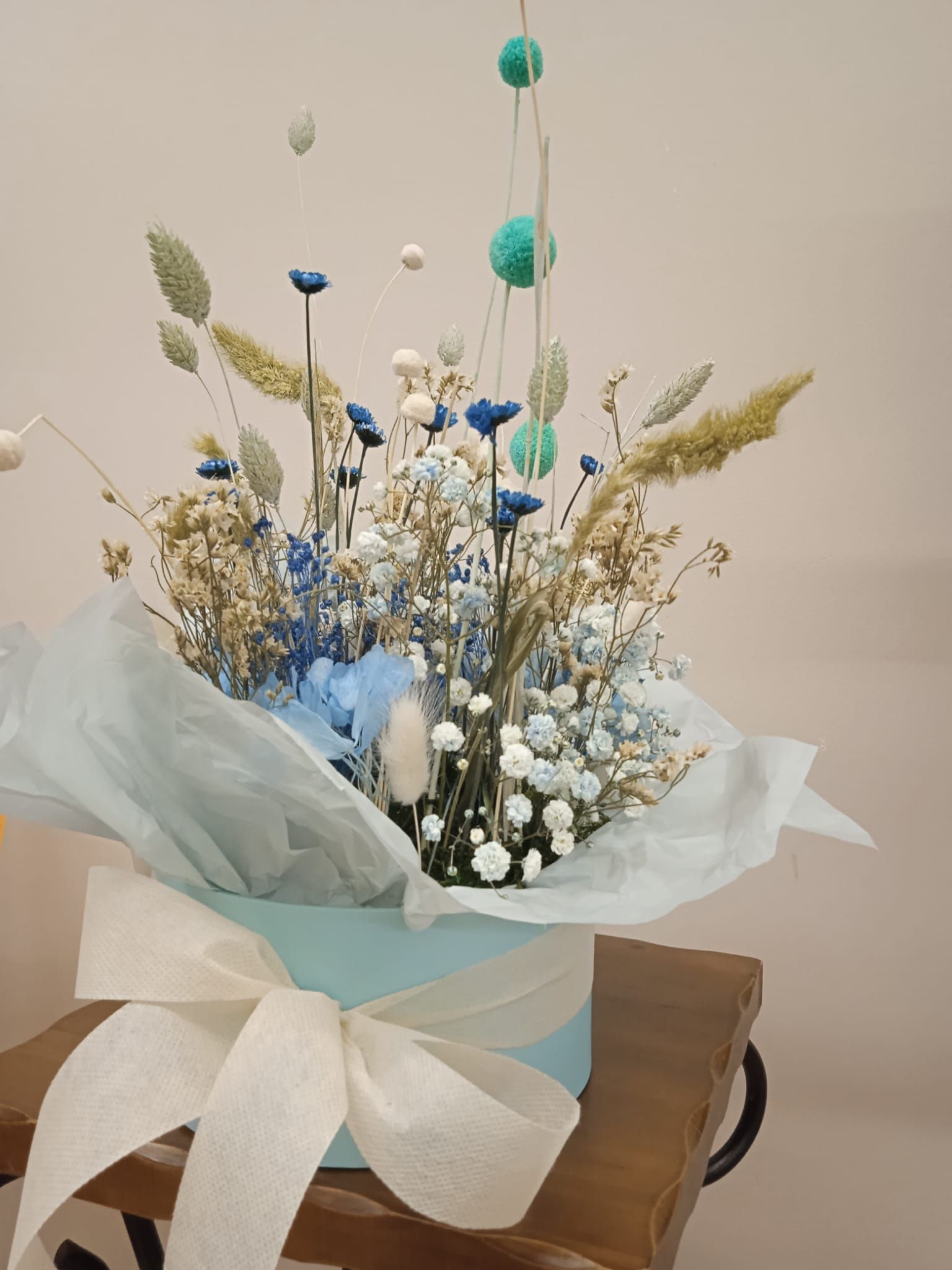Un jarrón lleno de flores secas y aliento de bebé está sobre una mesa de madera.