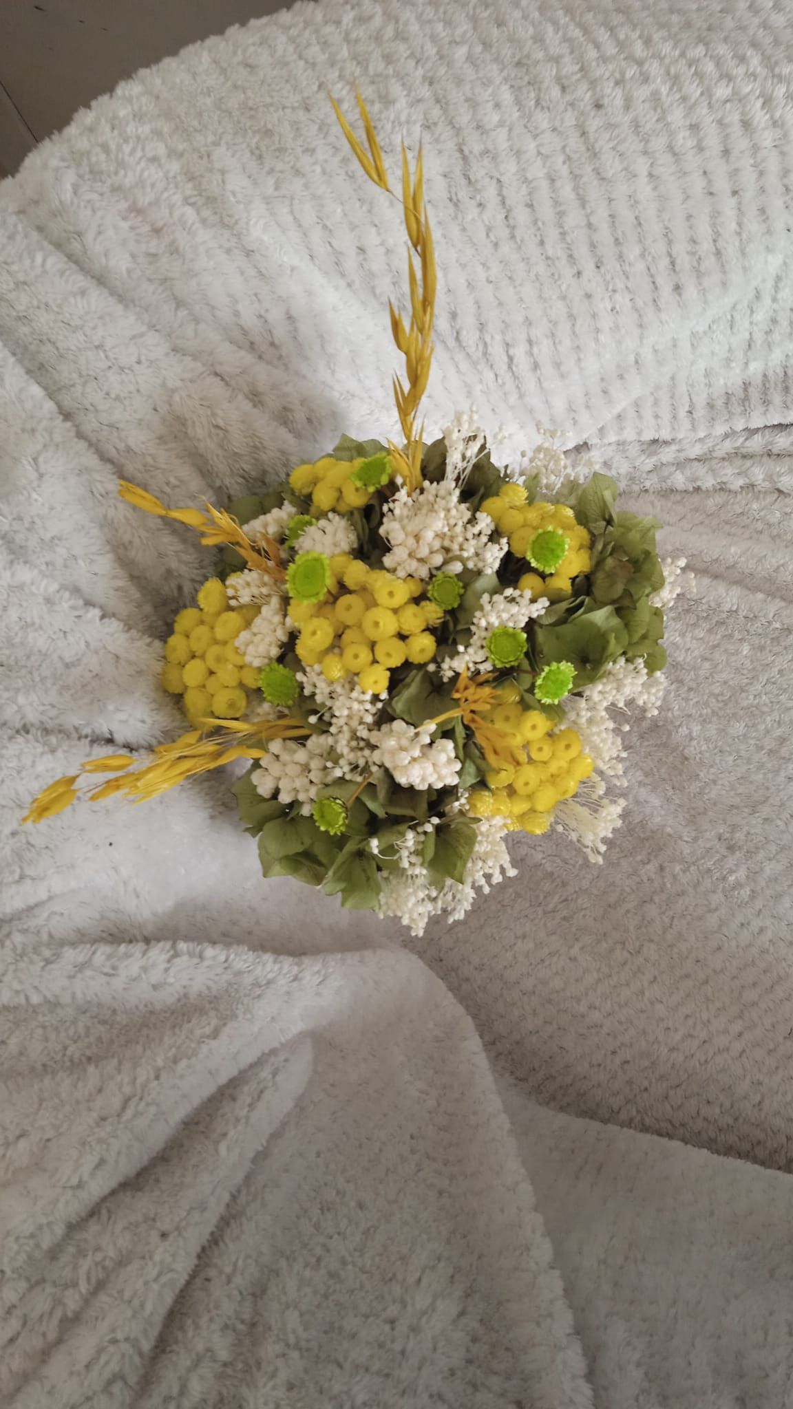 Un ramo de flores amarillas y verdes está sobre una manta blanca.