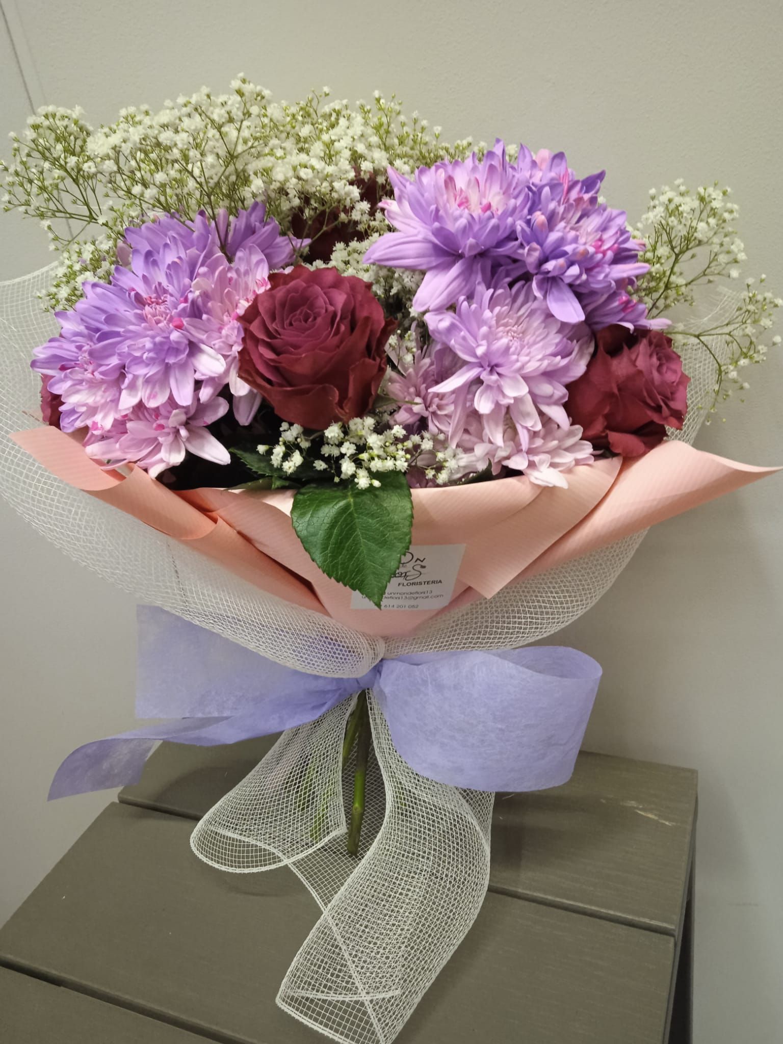 Un ramo de flores violetas con rosas y aliento de bebé envuelto en encaje.