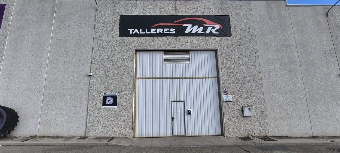 Exterior de un taller mecánico gris con una puerta de metal blanca y un letrero de “Talleres Mtz” encima.