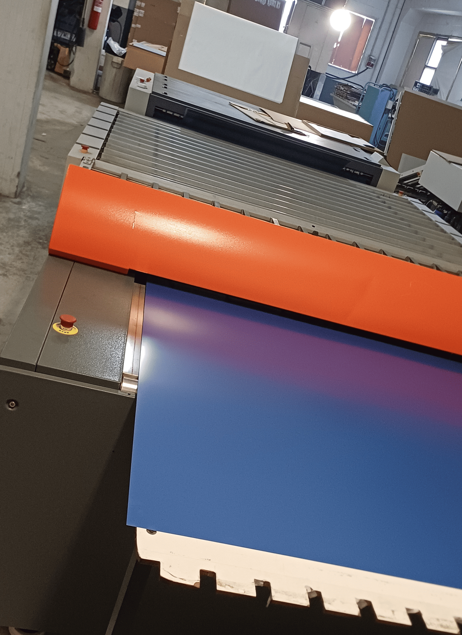 Una gran máquina de impresión enrolla una hoja con degradado azul-morado. Se ve un rodillo naranja. Ajuste de fábrica.