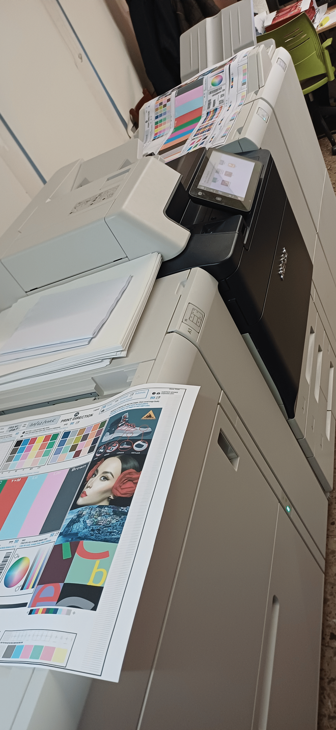 Una impresora a color de gran tamaño está imprimiendo una página de prueba con muestras de color y una imagen de una persona.