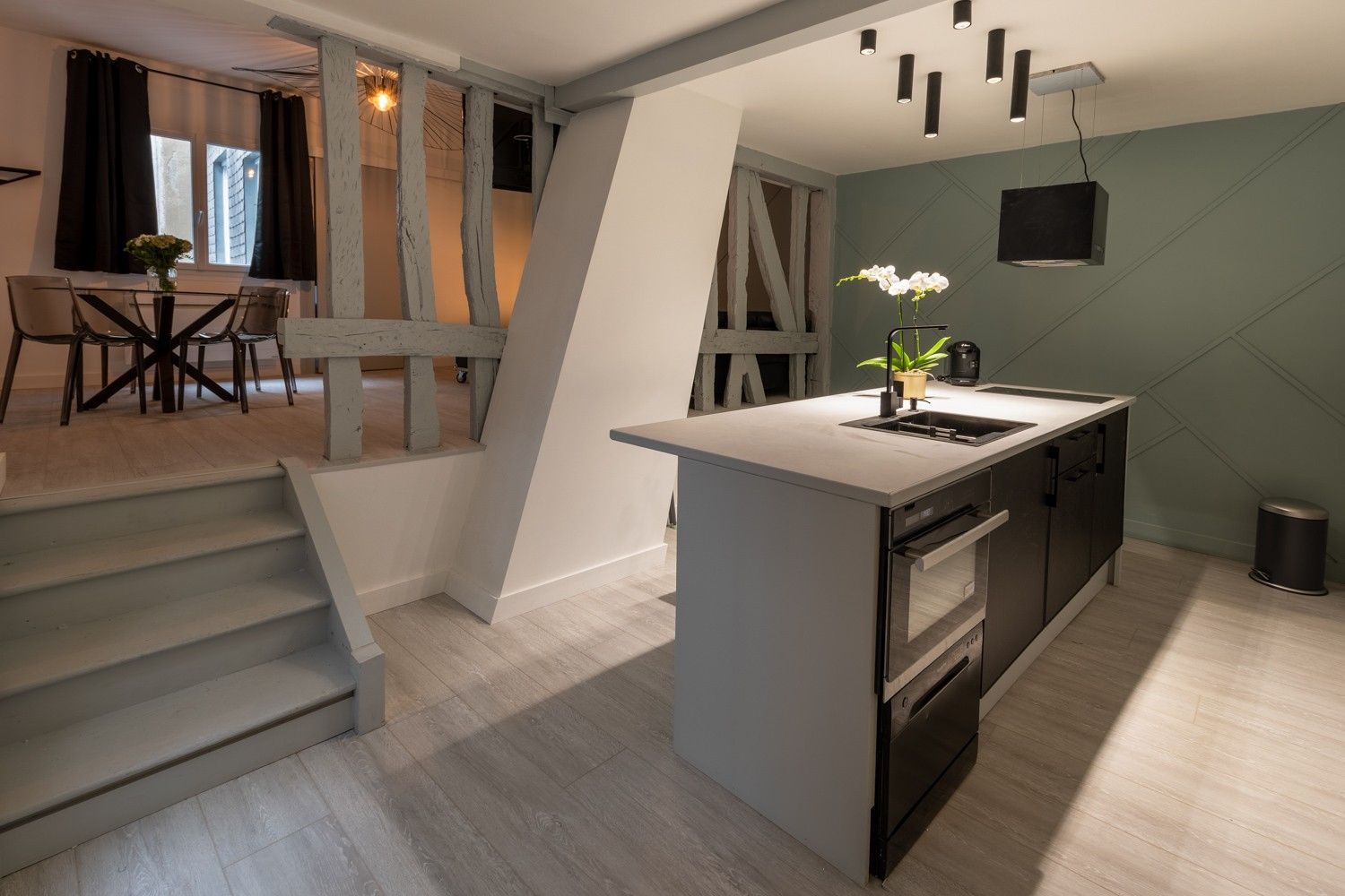 Cuisine ouverte en îlot centrale à proximité d'un petit escalier menant vers le salon.