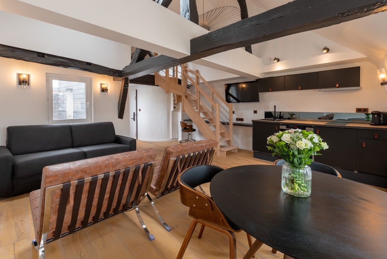 Intérieur d'un appartement avec salon salle à manger et cuisine ouverte dans les tons bois noir et marron.