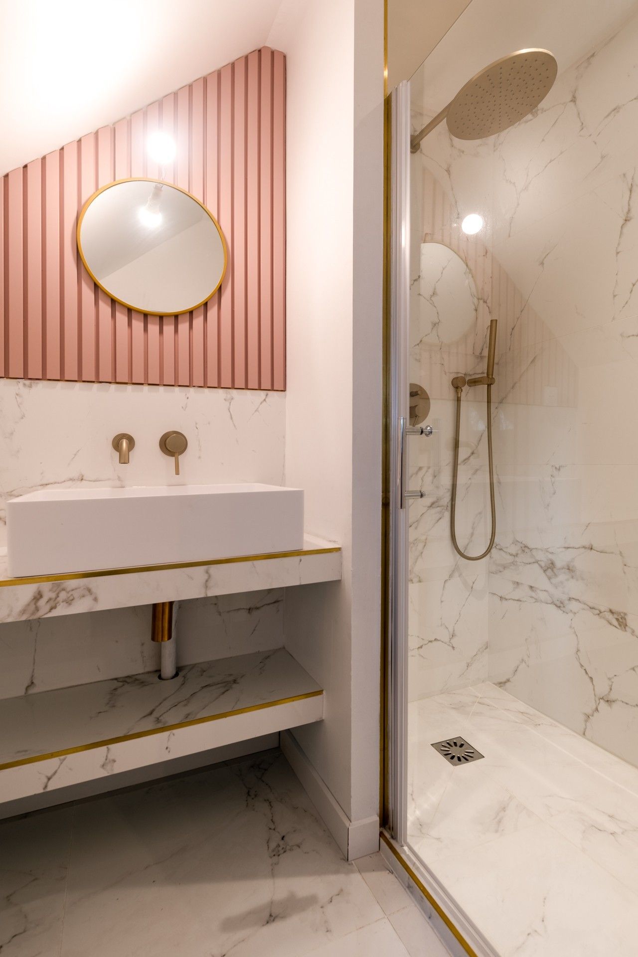 Salle de bains avec cabine de douche dans les tons de marbre et certain élément de couleur rose.