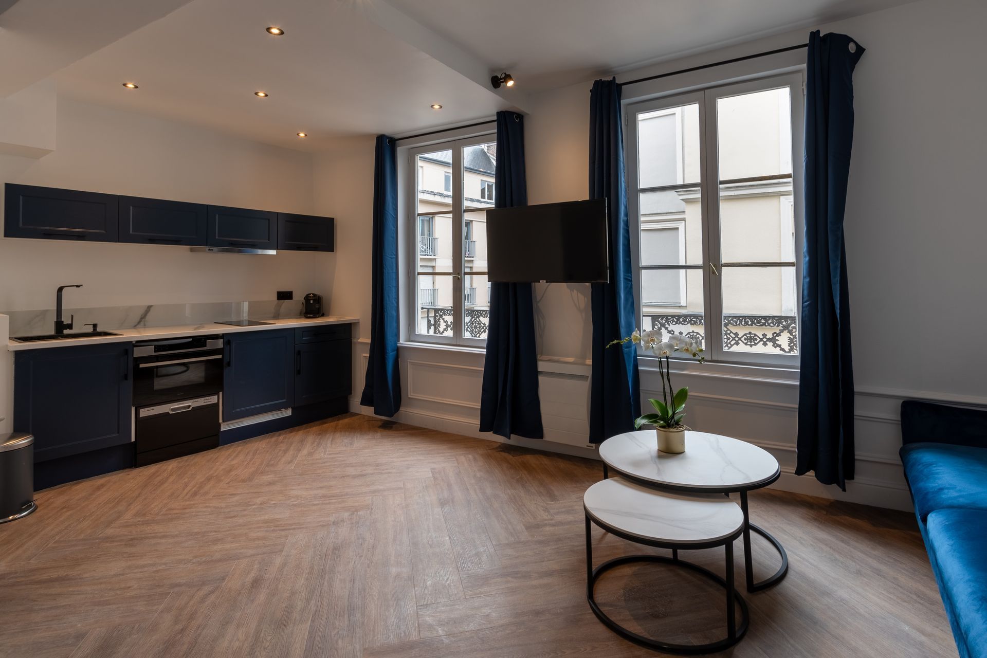 Grande pièce de cuisine et salon avec une télévision accrochée au mur entre deux fenêtres.