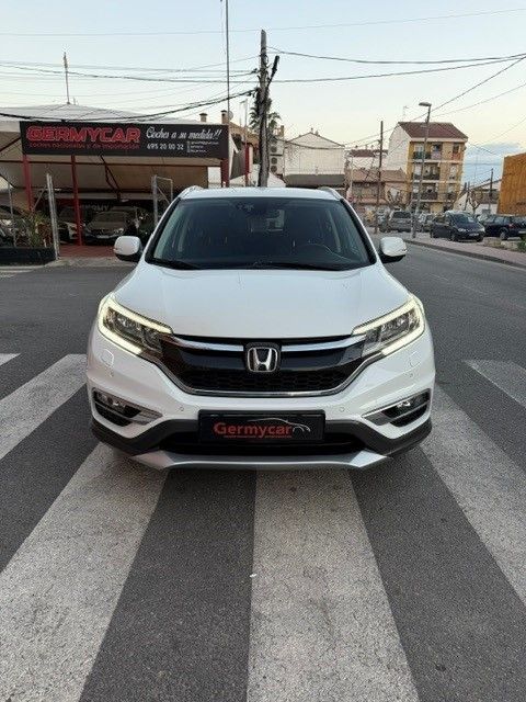 SUV Honda CR-V de color blanco en un cruce peatonal frente a un concesionario de automóviles, bajo un cielo despejado.