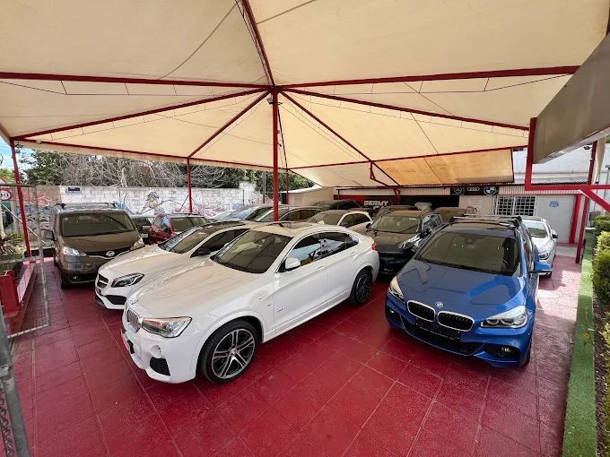 Coches aparcados bajo una marquesina. Un BMW X4 blanco está en el centro. El suelo es rojo.