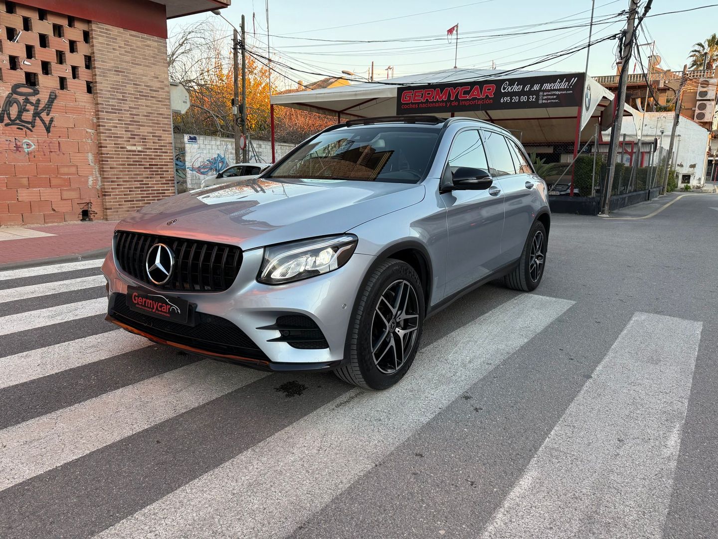 Un todoterreno Mercedes azul oscuro estacionado en un paso de peatones frente a un negocio de servicio de automóviles.