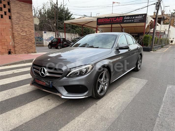 Un sedán Mercedes-Benz de color gris estacionado en una calle con un cruce de peatones frente a un lavadero de autos.