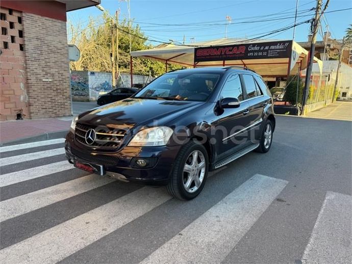 Un todoterreno Mercedes azul oscuro estacionado en un paso de peatones frente a un negocio de servicio de automóviles.