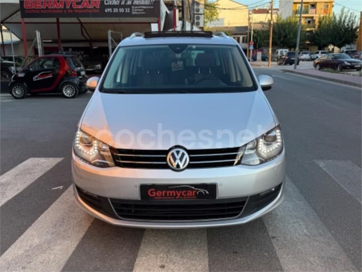Minivan Volkswagen Sharan color plata estacionada en una calle con una sala de exposición detrás.