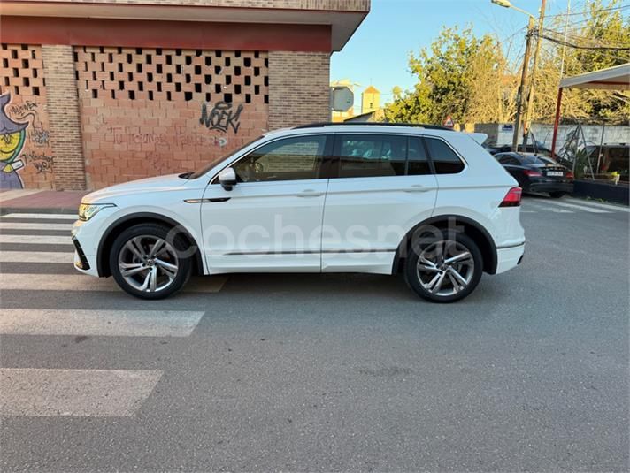 SUV Volkswagen Tiguan blanco estacionado en una calle de la ciudad frente a un edificio de ladrillos.