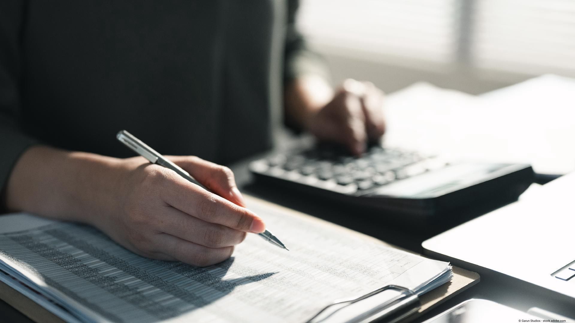 Person nutzt Taschenrechner und hält einen Stift über Dokumenten.