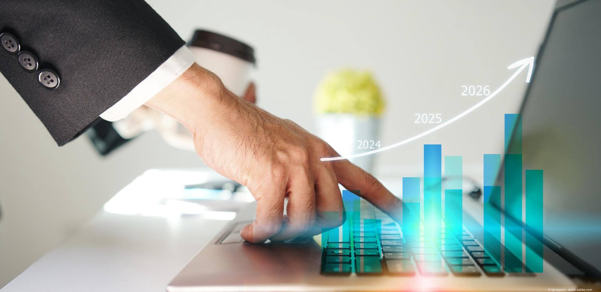 Hand zeigt auf ein Tablet mit steigenden Finanzgrafiken und Jahreszahlen.