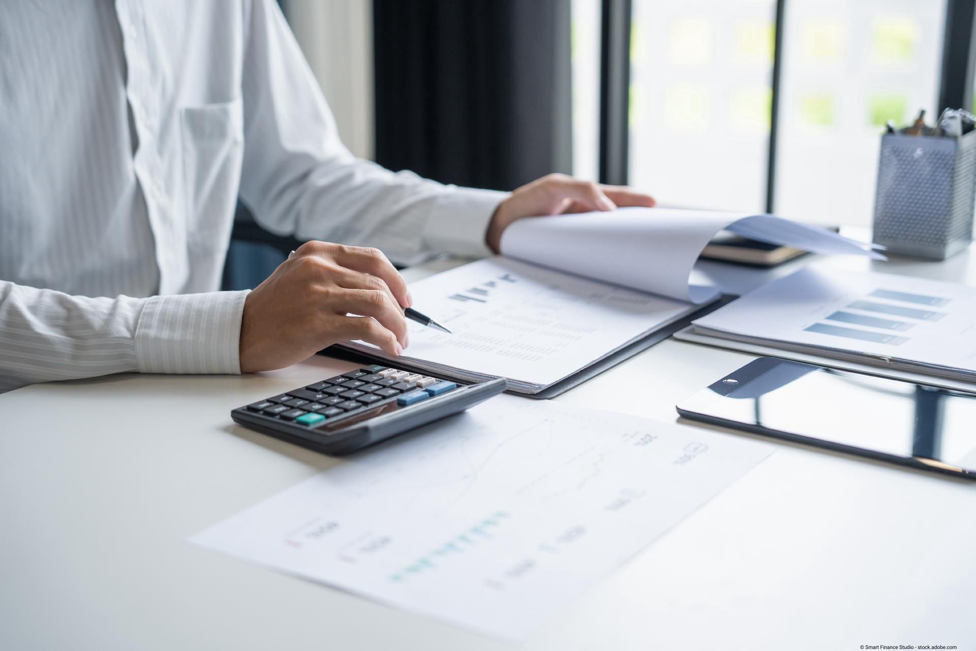 Geschäftsmann arbeitet mit Taschenrechner und Unterlagen am Schreibtisch.