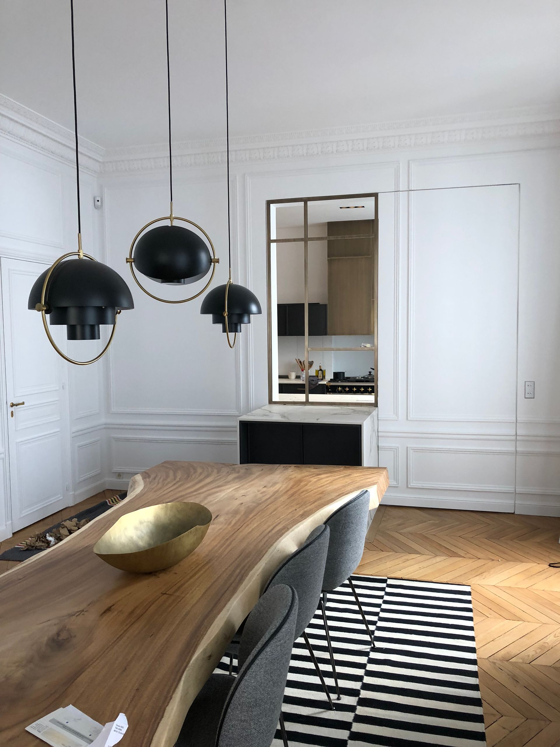 Salle à manger élégante avec murs lambrissés blancs, table en bois, suspensions lumineuses noires et tapis à rayures.