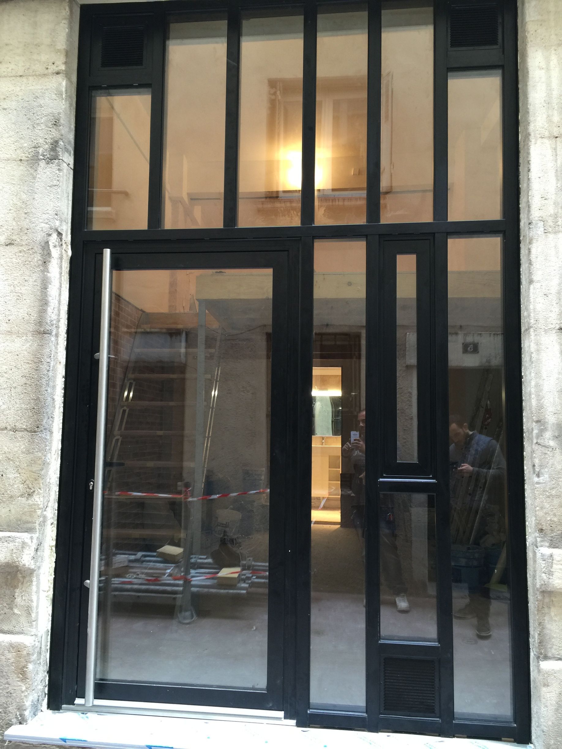 Façade vitrée avec encadrements en métal noir et intérieur éclairé se reflétant dans les vitrines.