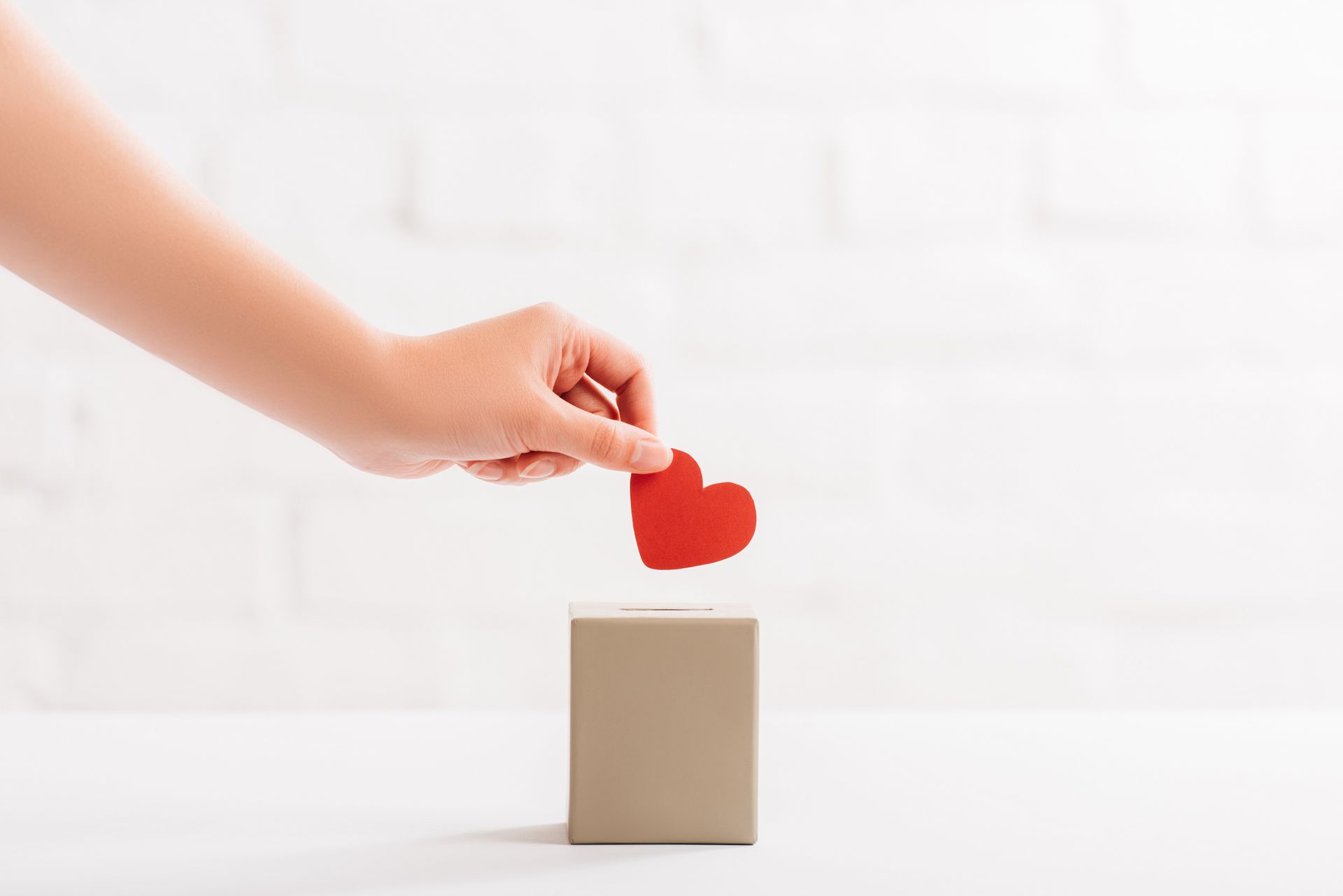 Spenden mit Herz – Eine Hand legt ein rotes Herzsymbol in eine Spendenbox.