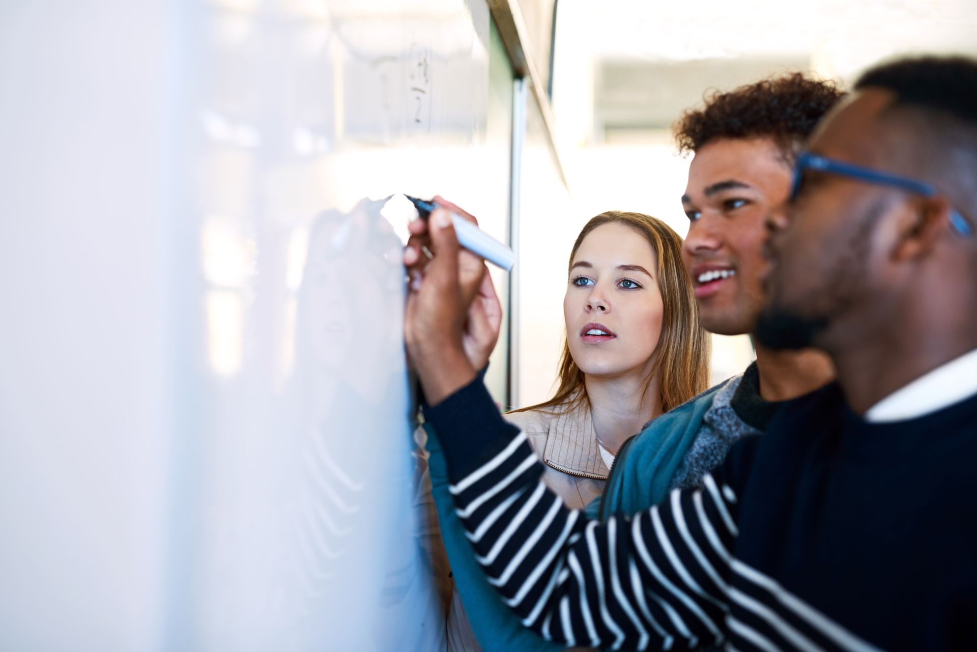 Gemeinsames Lernen – Drei junge Menschen arbeiten motiviert an einer Whiteboard-Aufgabe, Zusammenarbeit und Bildung im Fokus.