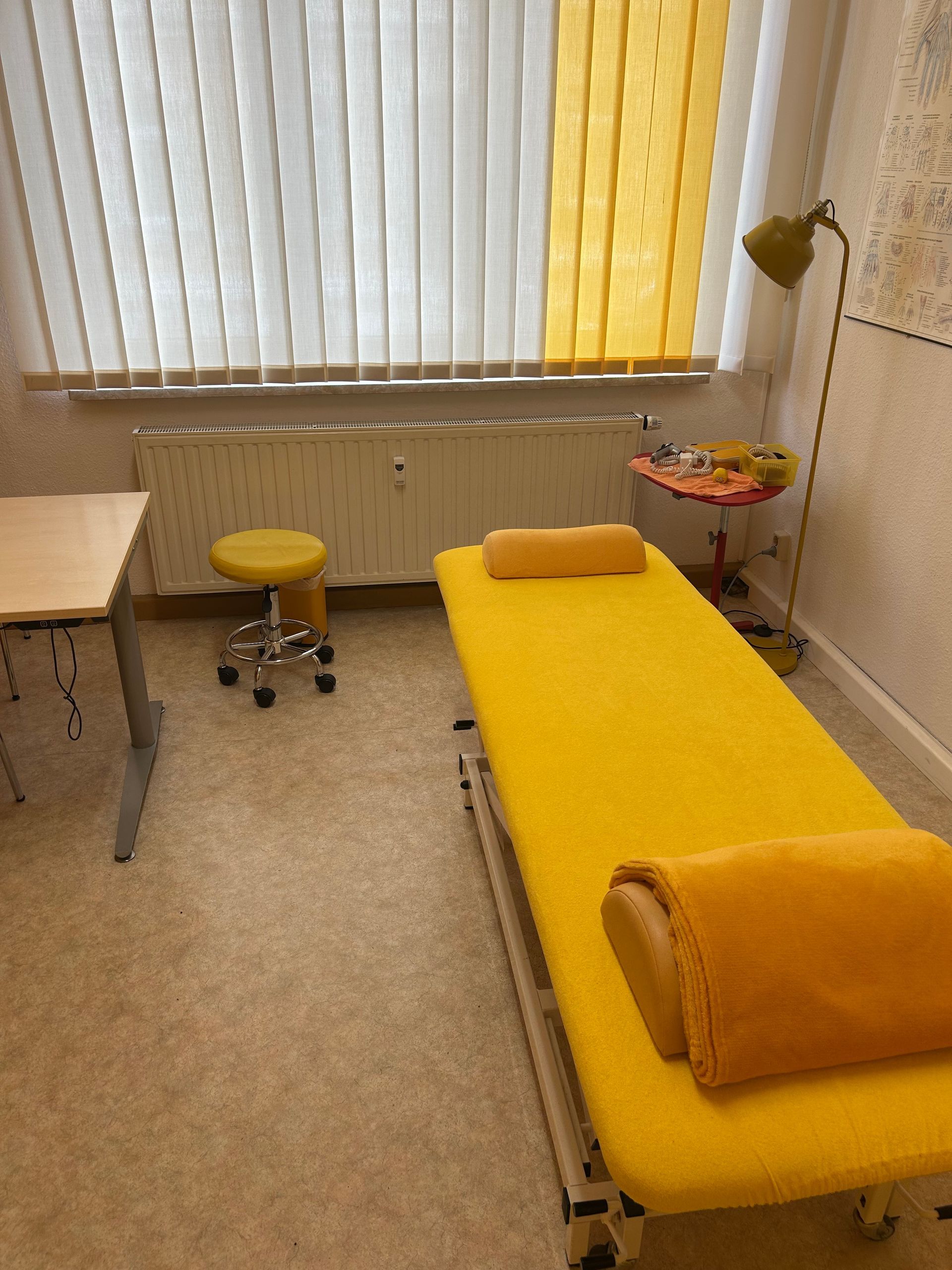 Behandlungszimmer mit Liege, Infopostern und Gardienen